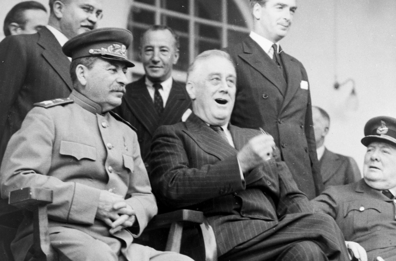 A vintage photo of a group of people sitting posing for the camera Description automatically generated